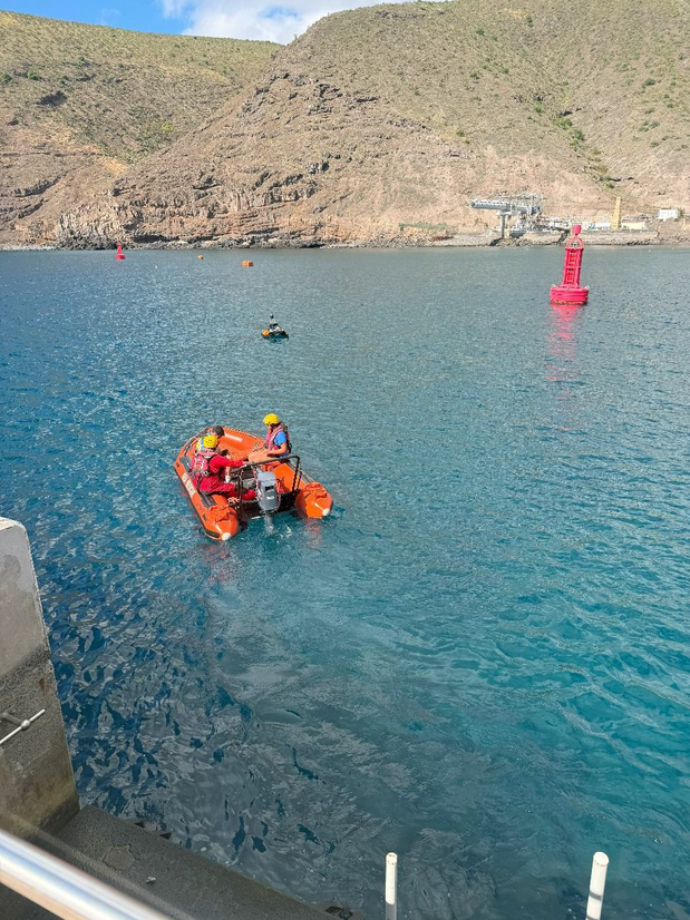 Three people aboard a small survey boat in a harbour following a uncrewed surface vessel.